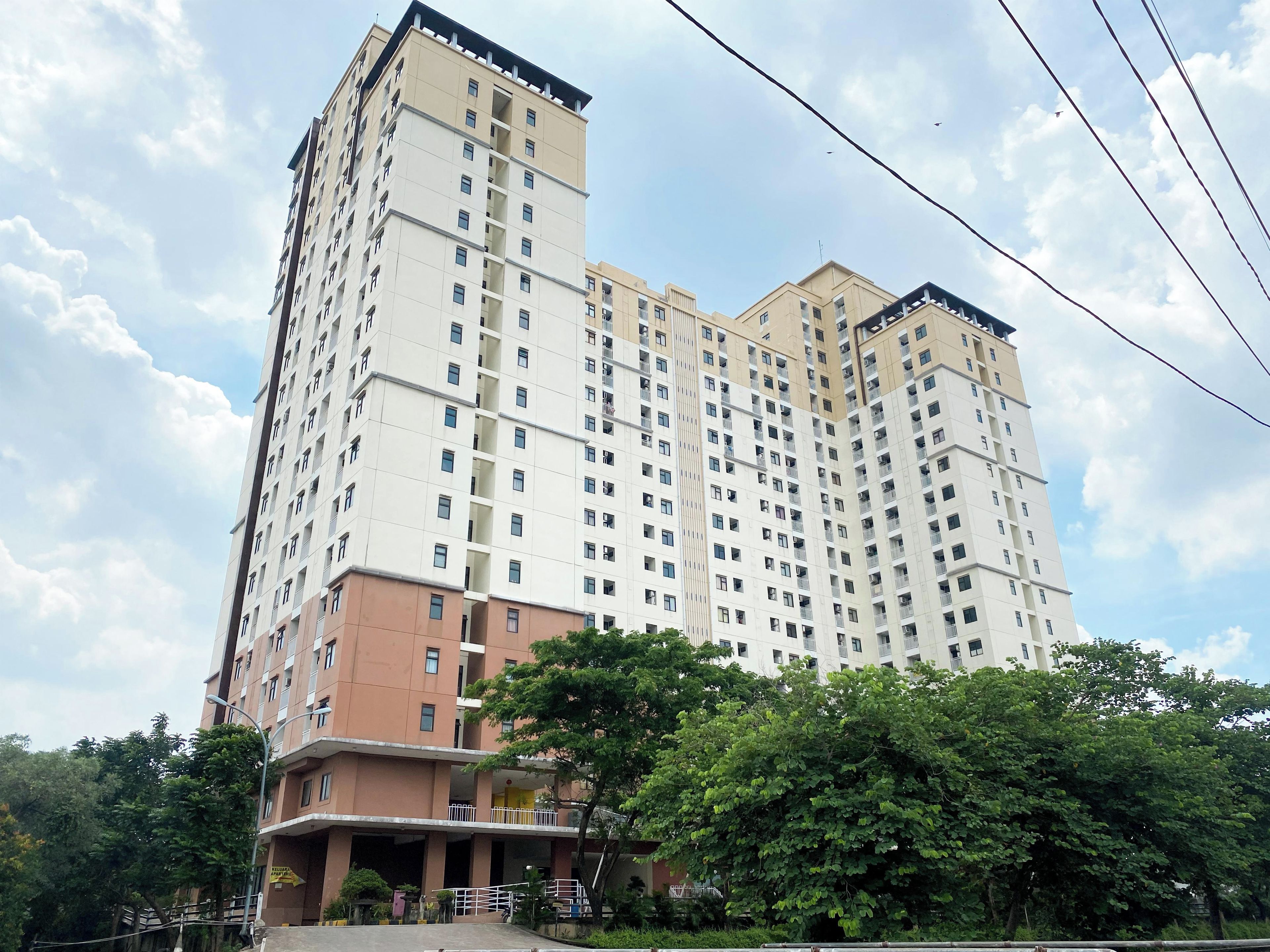 Un edificio residencial de varios pisos con balcones, entrada protegida y zona verde circundante.