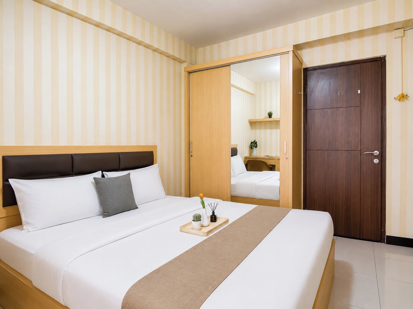 Una habitación de hotel con cama, un armario de madera, un espejo y una mesita con bandeja.