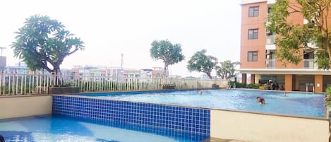 Una piscina con borde de azulejos, rodeada de una valla y árboles.