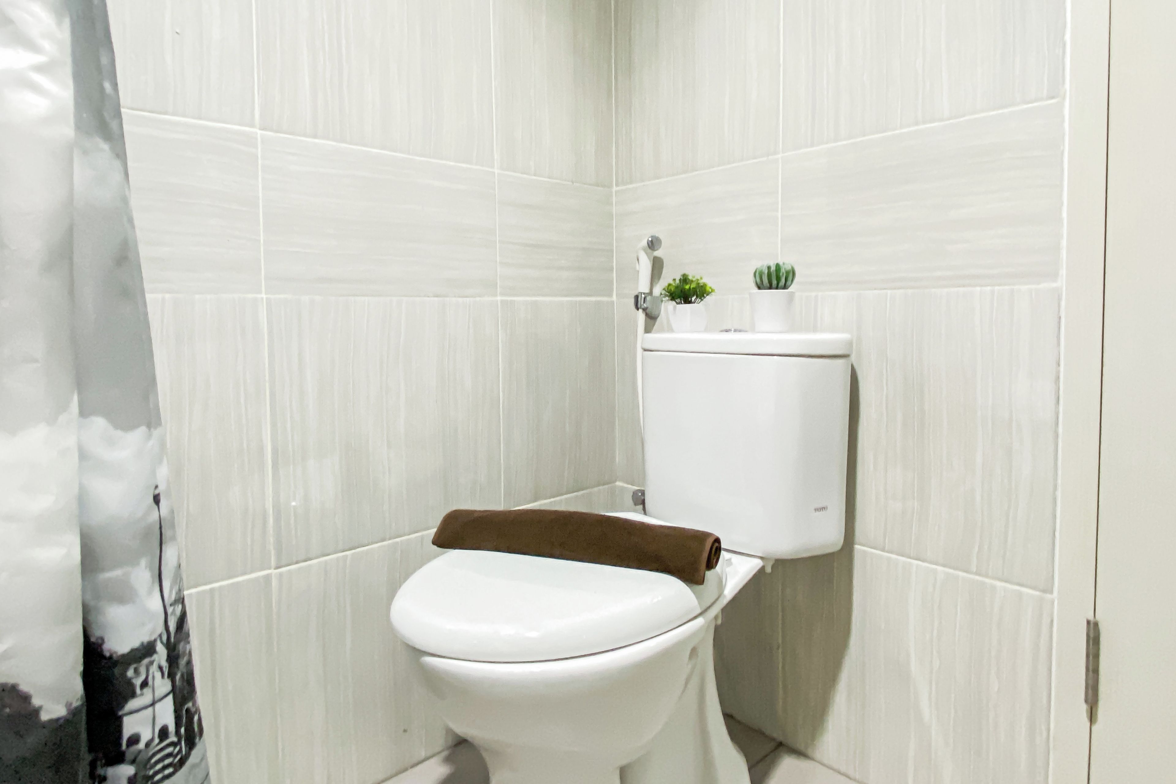 Eine kleine, weiße Toilette mit einem braunen Handtuch auf dem Sitz, einem Toilettenpapierhalter und einem kleinen Blumentopf auf dem Tank.