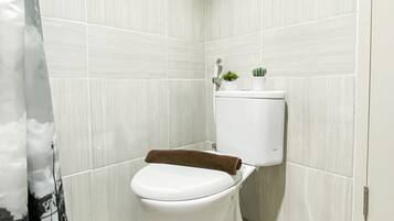 Eine kleine, weiße Toilette mit einem braunen Handtuch auf dem Sitz, einem Toilettenpapierhalter und einem kleinen Blumentopf auf dem Tank.