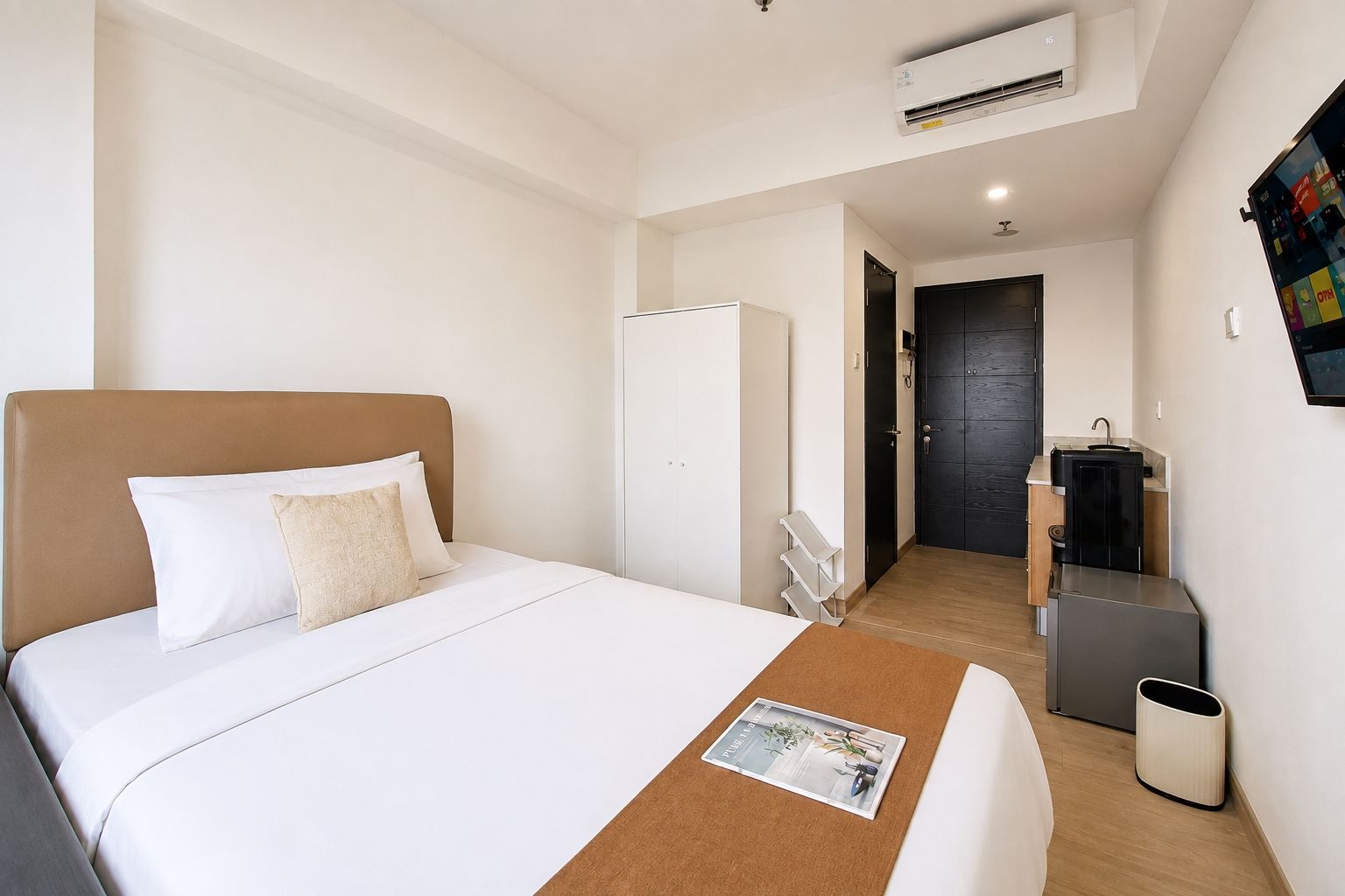 Una camera d'albergo con un letto, un piccolo tavolino con una rivista, una scrivania con un computer, un armadio e un bagno con uno specchio e un lavandino.