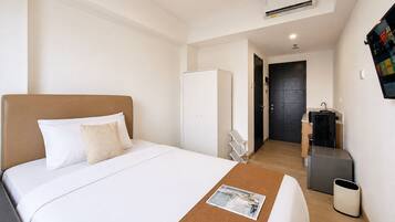 Una camera d'albergo con un letto, un piccolo tavolino con una rivista, una scrivania con un computer, un armadio e un bagno con uno specchio e un lavandino.