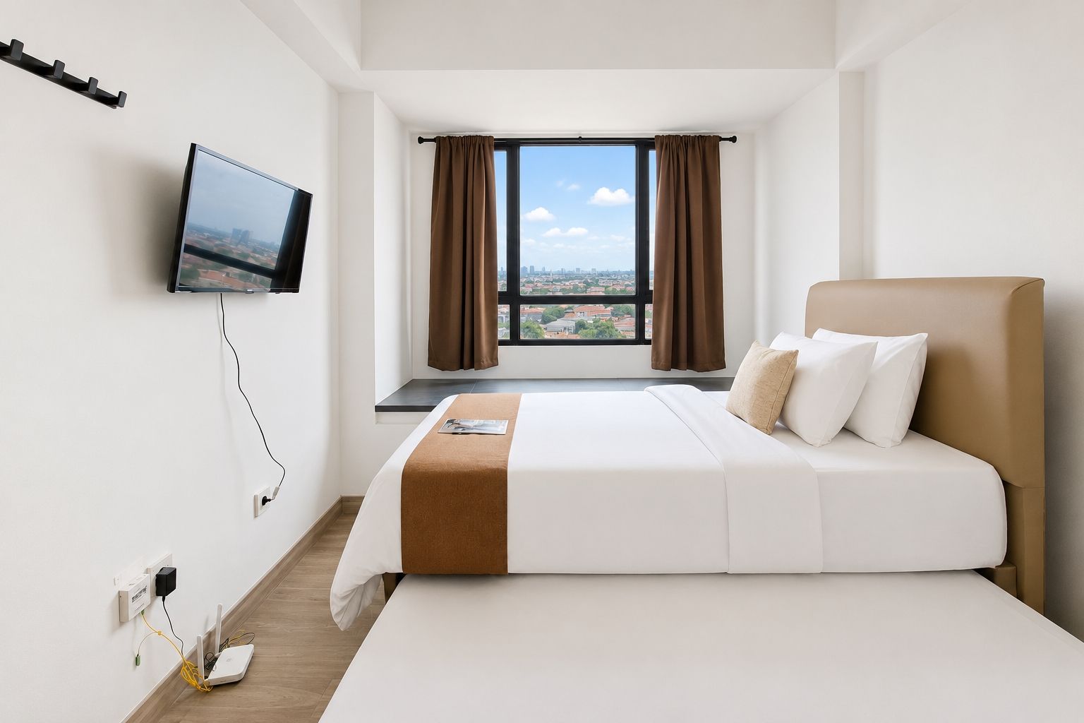 Una camera d'albergo con un letto, una televisione a parete, una finestra con tende e vista sulla città.