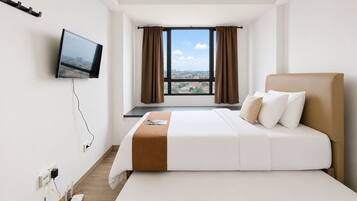 Una camera d'albergo con un letto, una televisione a parete, una finestra con tende e vista sulla città.