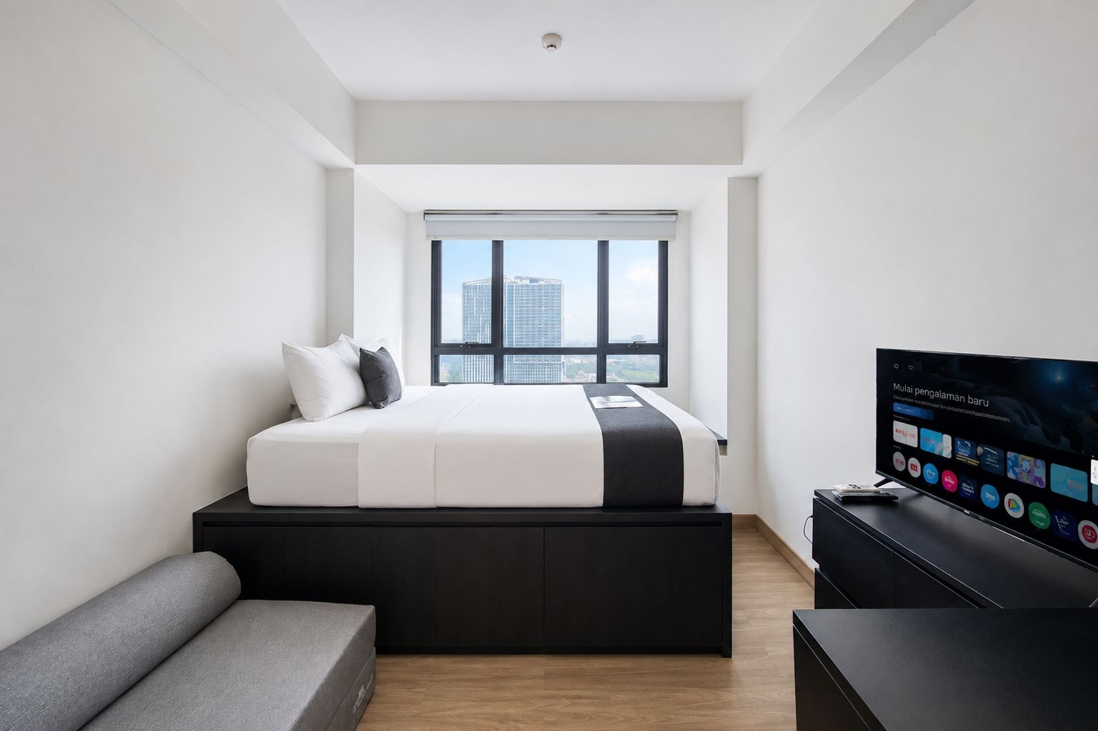 Un dormitorio moderno con cama, televisor y ventana con vista a la ciudad.