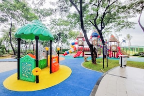 Ein Spielplatz mit bunten Spielgeräten, darunter Rutschen und Kletterbereiche, umgeben von Bäumen.