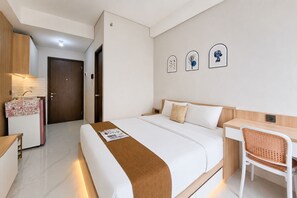 A hotel room with a bed, a desk, a chair, a kitchenette, and a door. - Bright And Airy Studio At Apartment Transpark Bintaro (Tangerang)