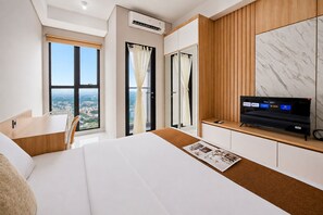 Ein Hotelzimmer mit Bett, Schreibtisch, Fernseher und Blick auf die Stadt.