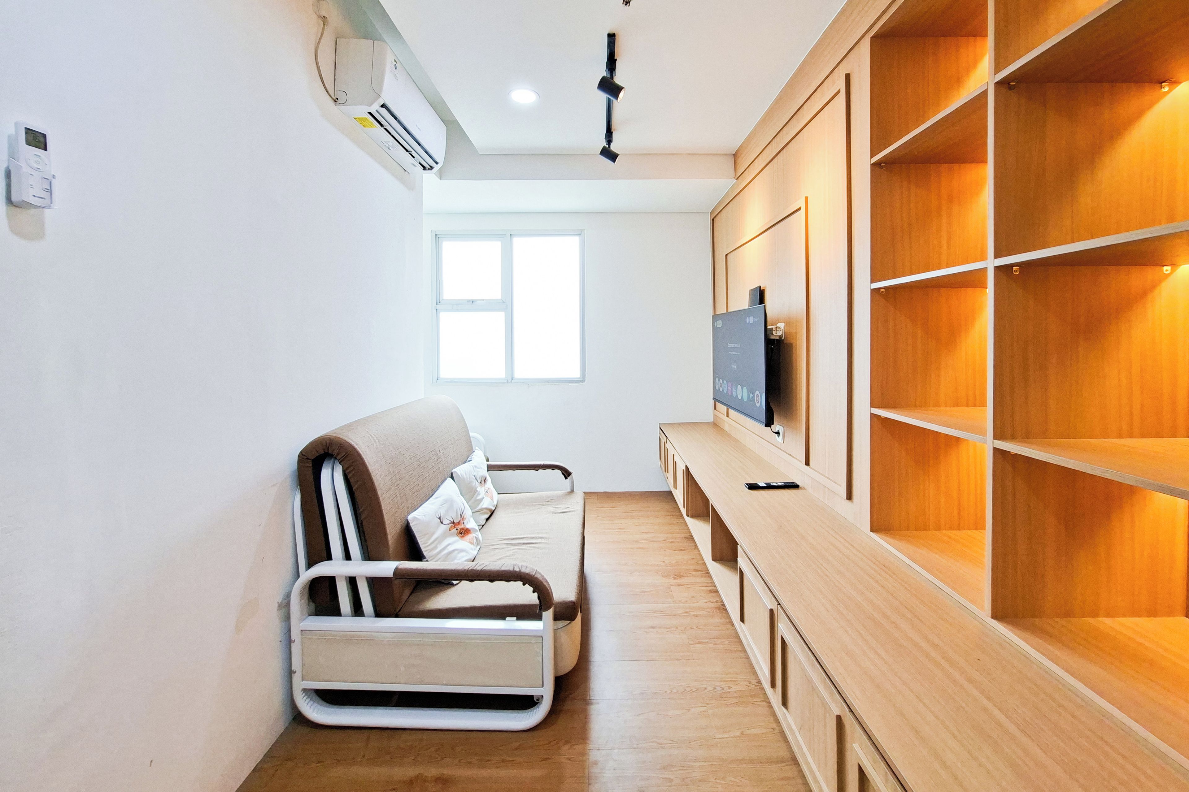 A modern room with a sofa, a TV on a wooden cabinet, and a window.
