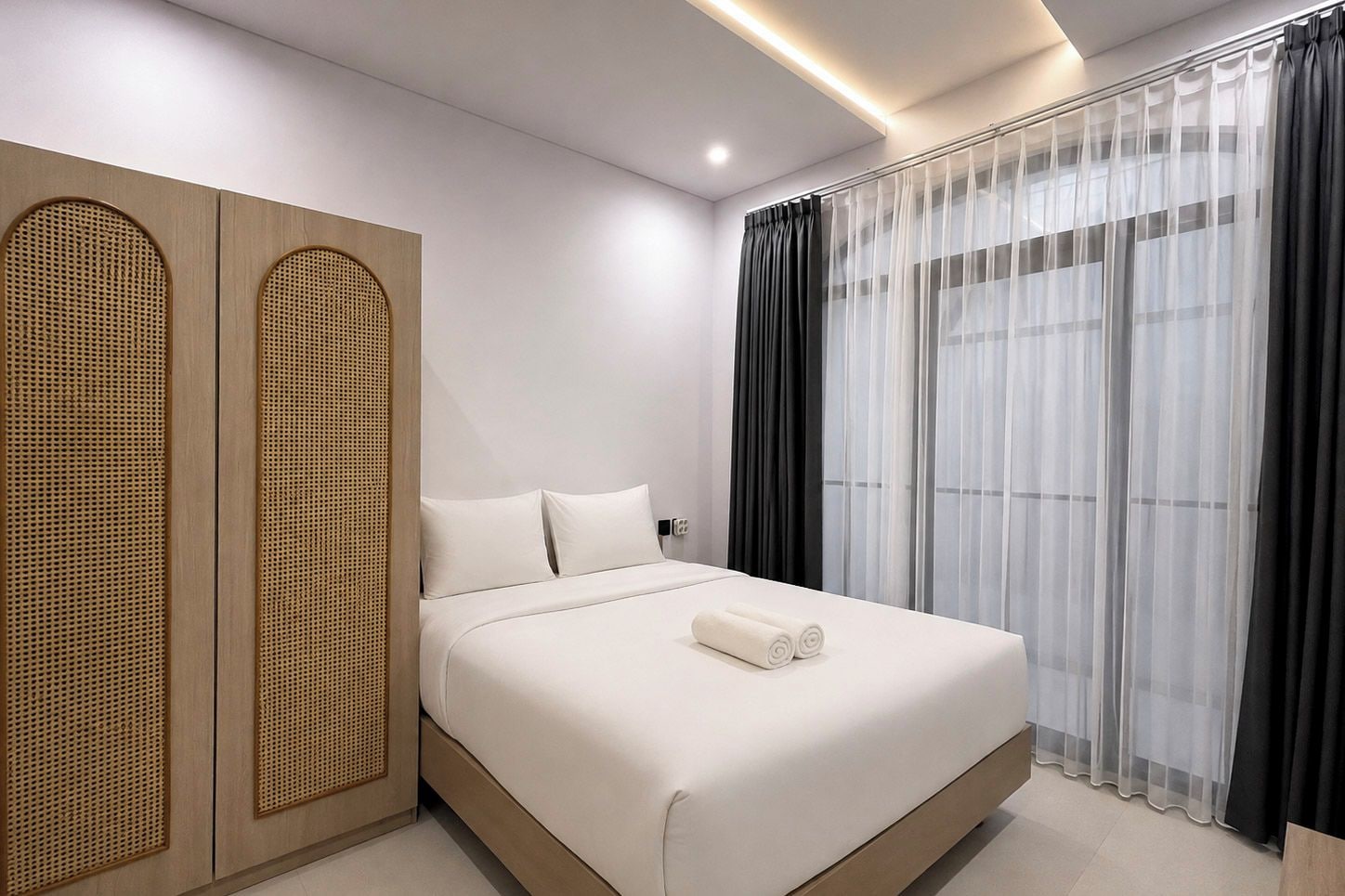 Een moderne hotelkamer met een groot bed, een inloopkast met geweven motief en dunne gordijnen.