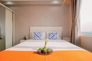 A hotel room with a bed, two pillows, a nightstand, a potted plant, and a window with curtains.