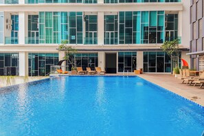A modern hotel with a swimming pool, lounge chairs, and a large glass facade. - Affordable Neat 1Br At Apartment Brooklyn Alam Sutera (Tangerang)