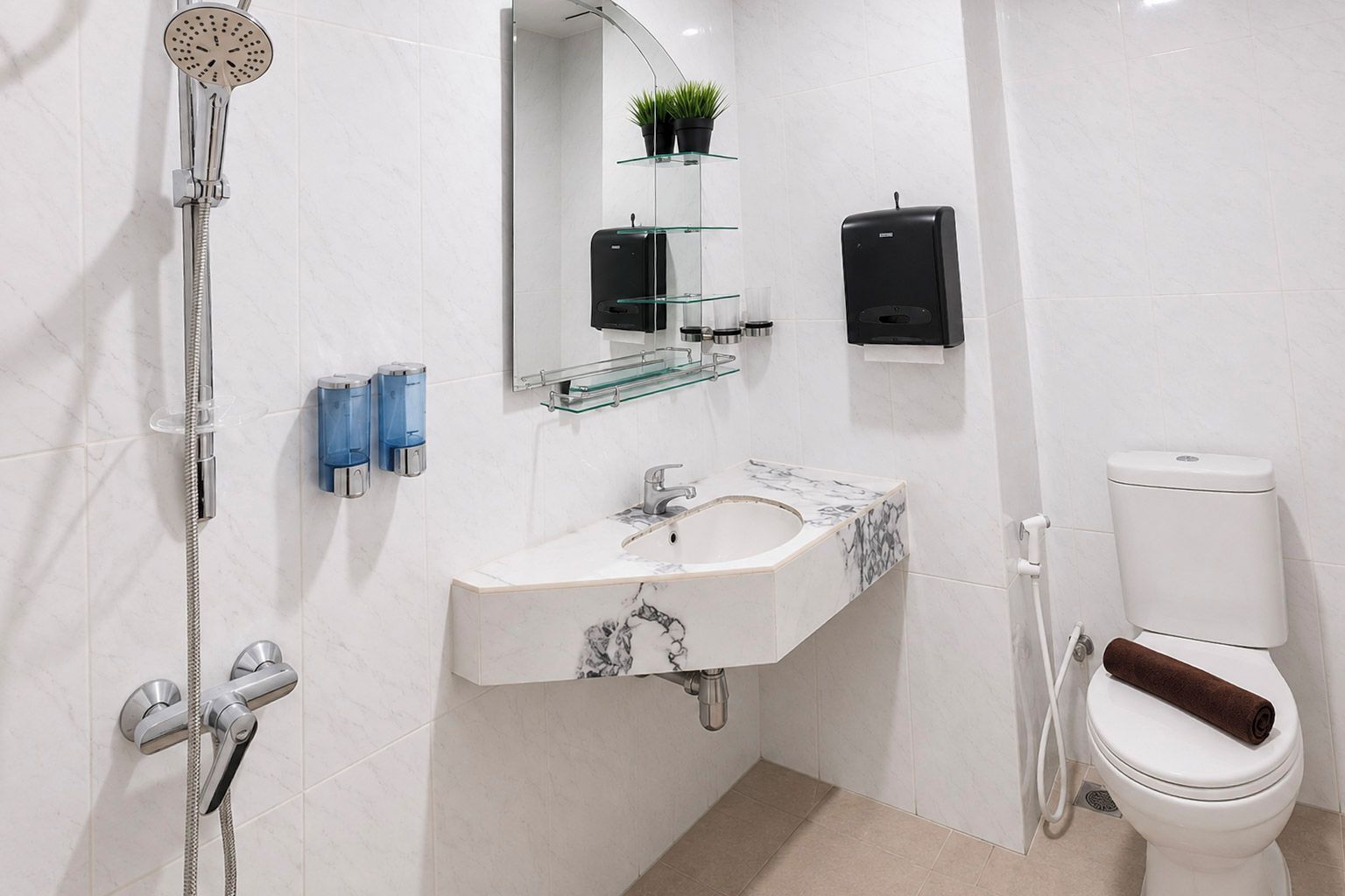 Un baño moderno con ducha, lavamanos, inodoro y estantes de vidrio con plantas.