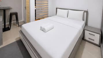 A modern hotel room with a large bed, a small bedside table with drawers, a desk with a chair, and a sliding door with a patterned curtain.