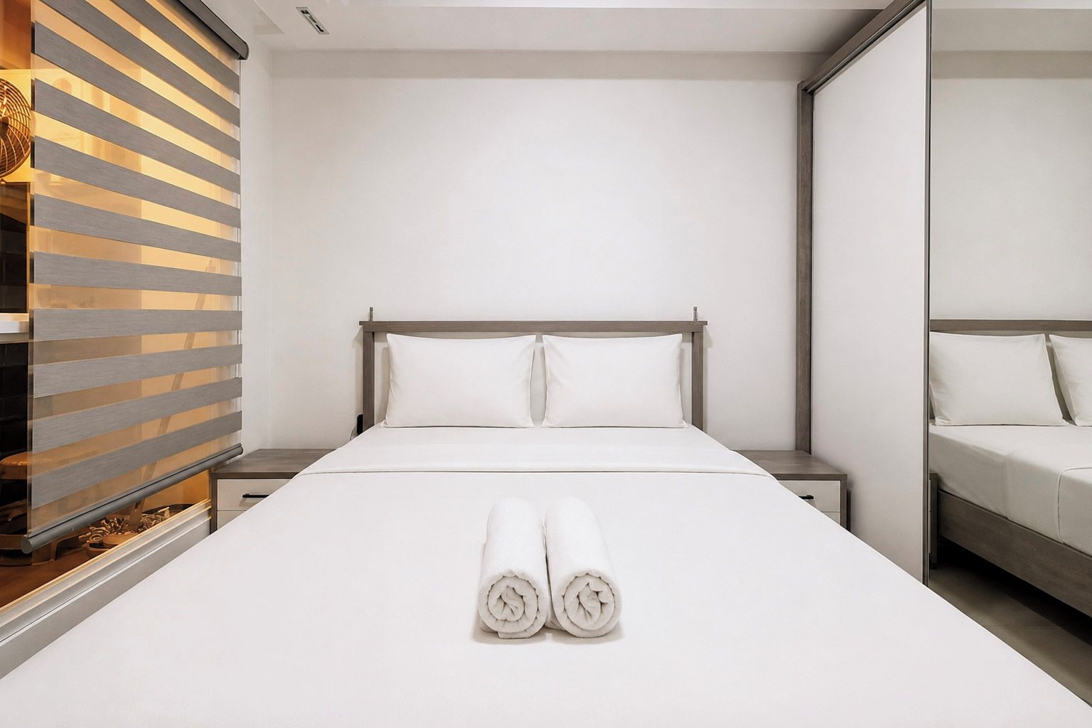 A hotel room with a large bed, a wooden headboard, two nightstands, and a mirror on the wall.