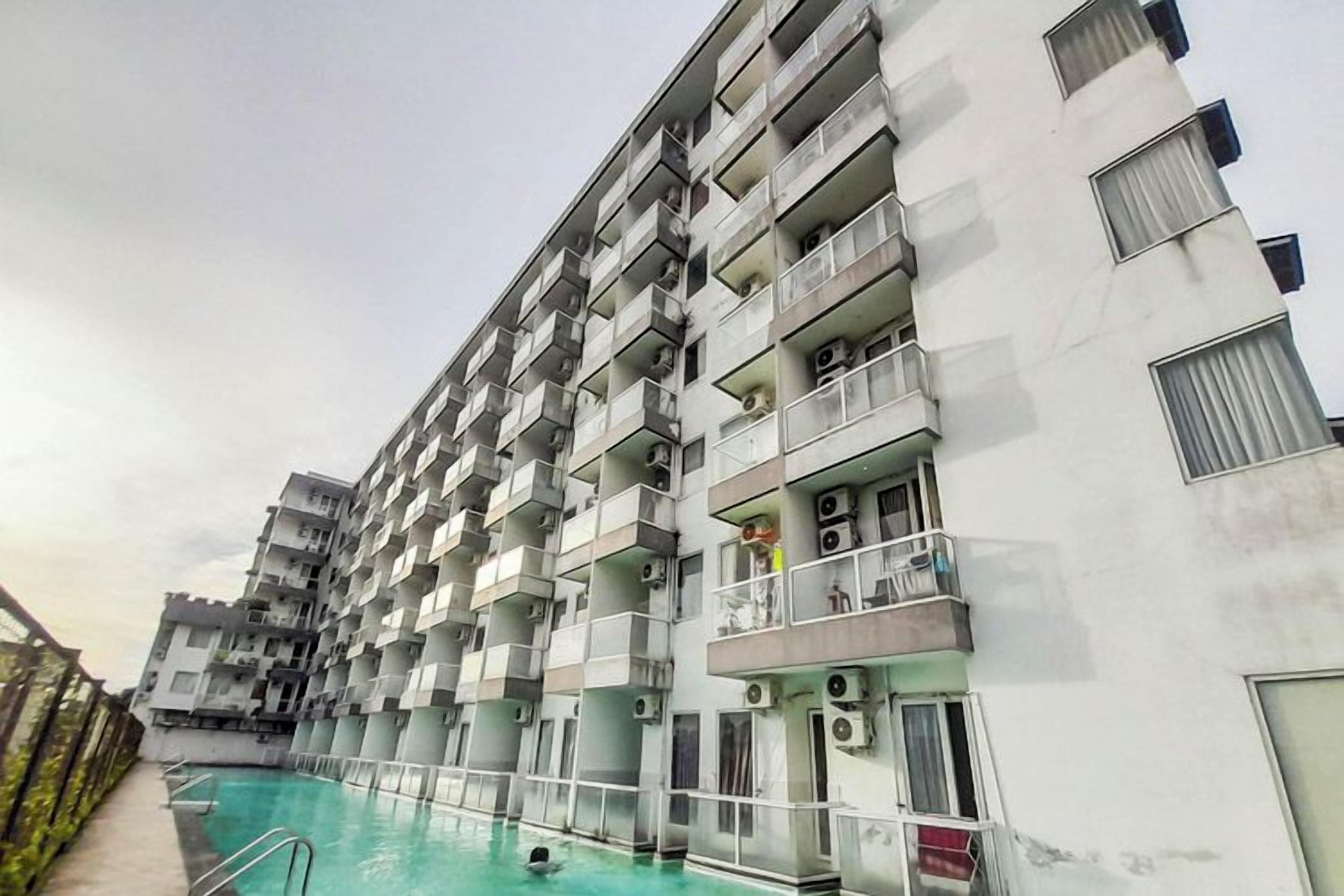 A multi-story hotel with balconies, a swimming pool, and a clear sky.