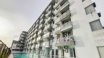 A multi-story hotel with balconies, a swimming pool, and a clear sky.
