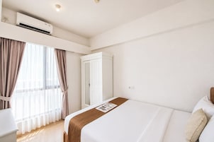 Ett hotellrum med en säng, en garderob, ett element och ett fönster med gardiner.