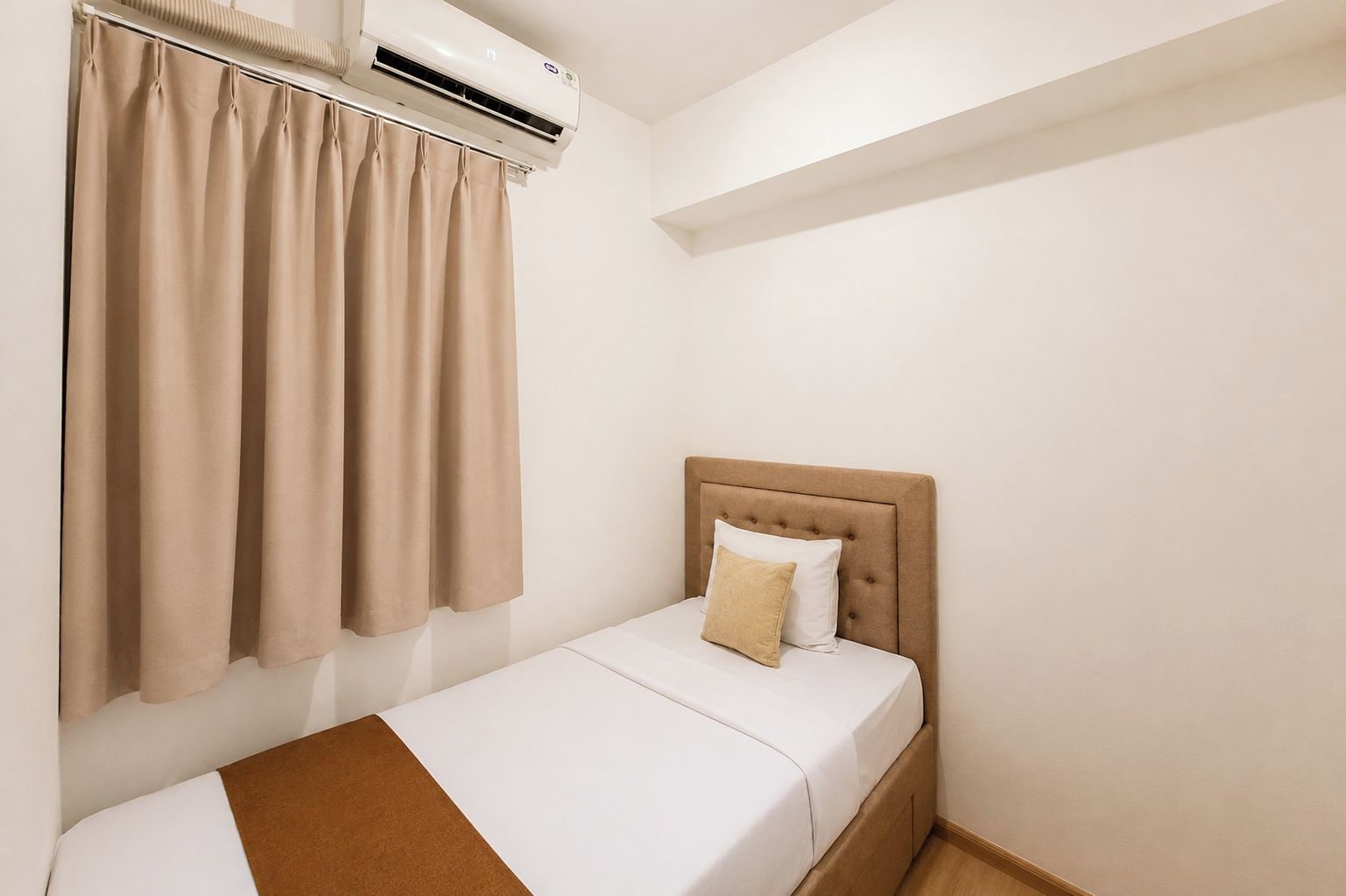 A single bed with a headboard, a window with curtains, and an air conditioning unit mounted above the window.
