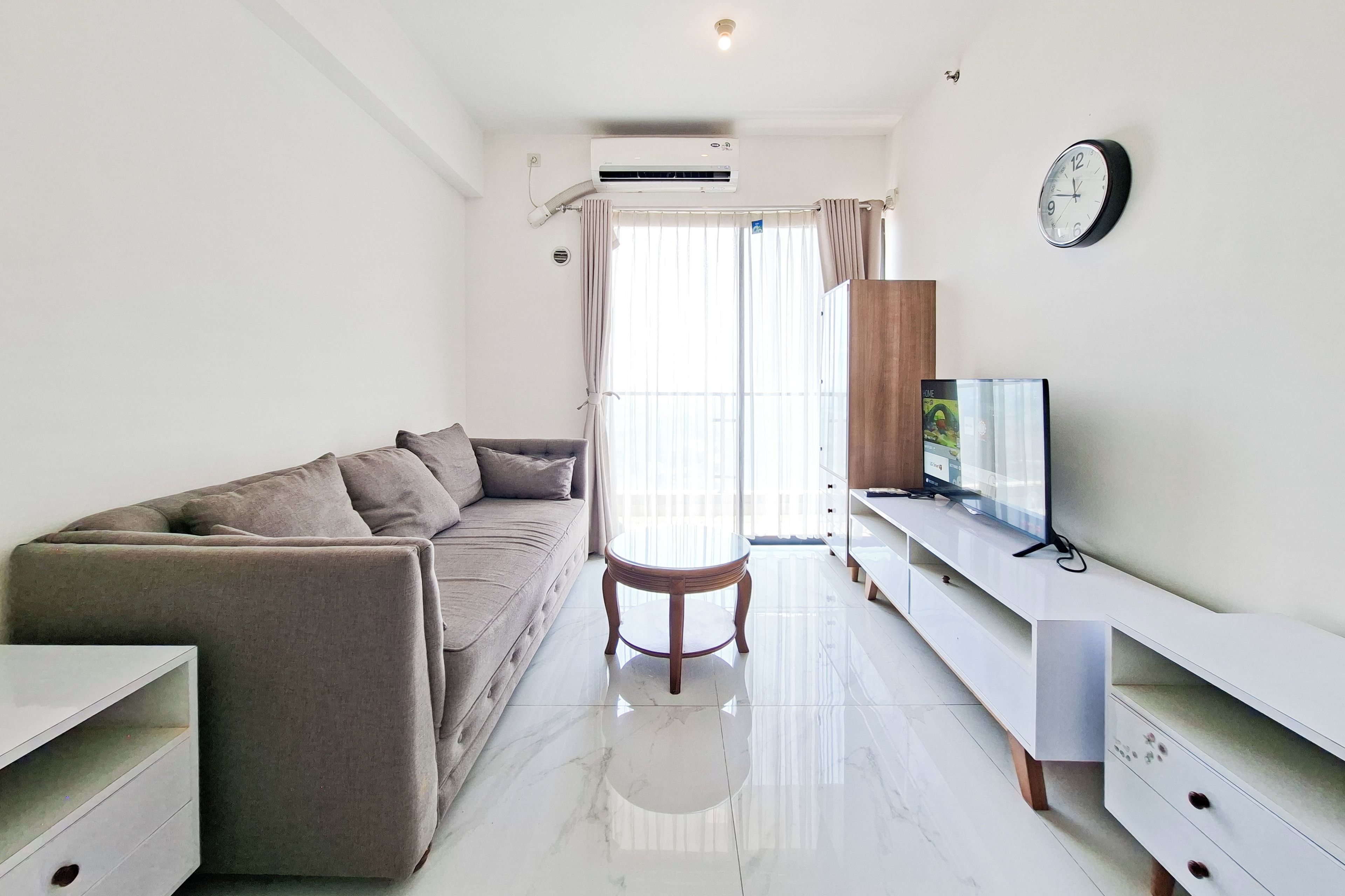 A modern living room with a sofa, a TV on a stand, and a large window with curtains.