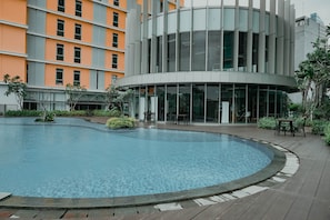 A modern building with a circular pool, outdoor seating, and a glass facade. - Warm And Sleek 1Br At Apartment Pejaten Park Residence (Jakarta)