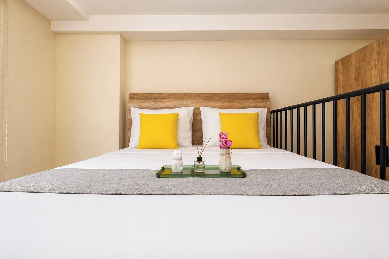 A hotel room with a bed, two pillows, a bedside table with a vase and a figurine, and a wooden headboard.