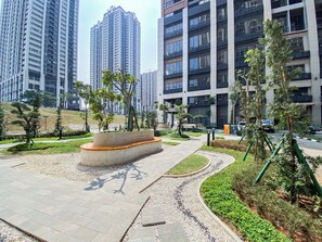 A modern urban residential area with high-rise buildings, landscaped gardens, and a paved walkway. - Warm And Peaceful 2Br At Apartment Meikarta District 1 (Cikarang)