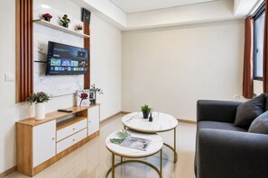 Uma sala de estar moderna com televisão de tela plana na parede, um sofá cinza, duas mesas de centro redondas e um armário de madeira com gavetas.