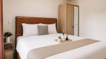 A neatly made bed with a wooden headboard, a bedside table with a vase of flowers, and a wooden tray with a plant and a candle.