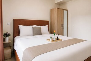 Uma cama bem arrumada com cabeceira de madeira, uma mesa de cabeceira com um vaso de flores e um tabuleiro de madeira com uma planta e uma vela.