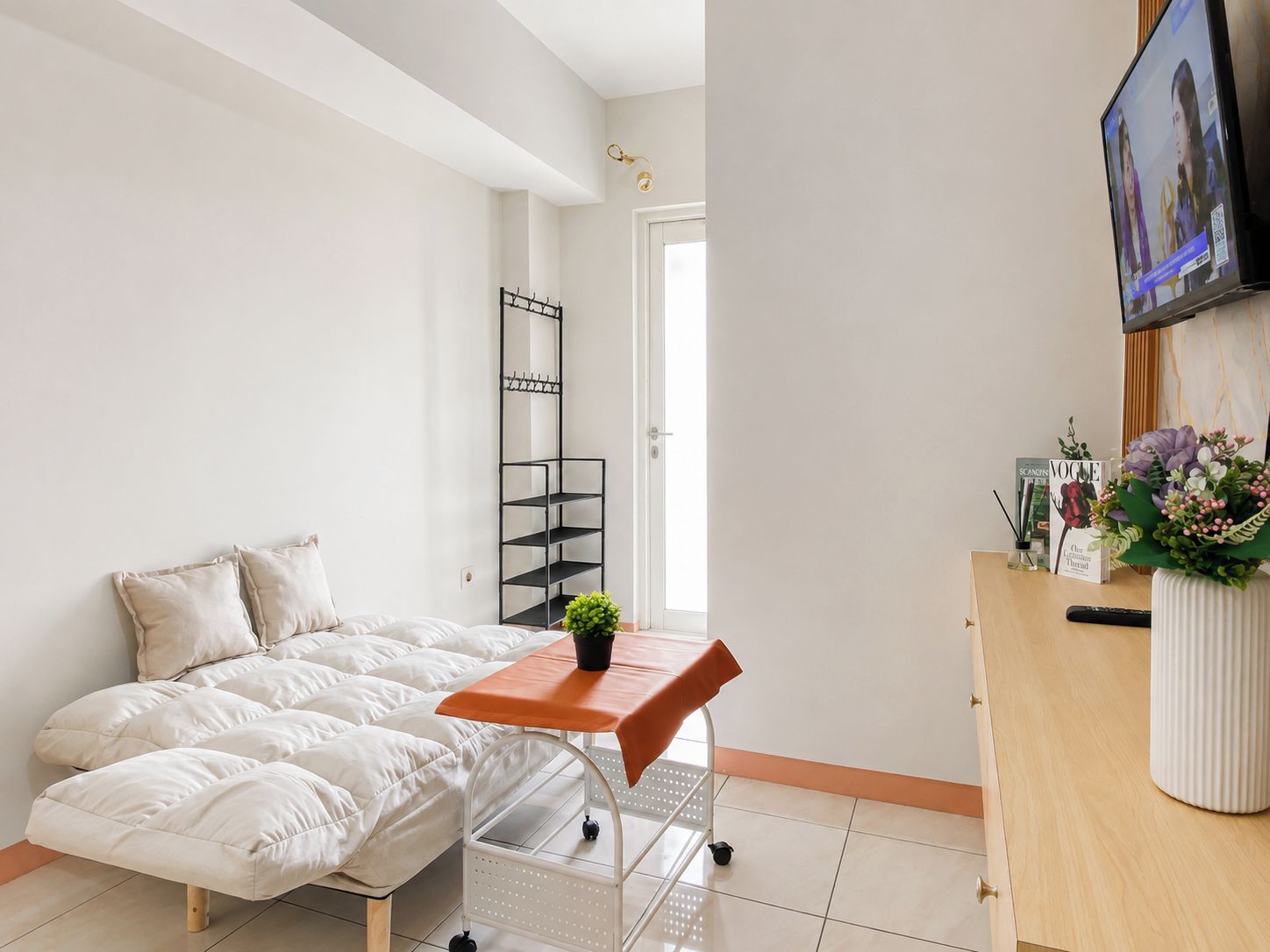A bedroom with a bed, a small table, a mirror, a TV, and a door leading to another room.