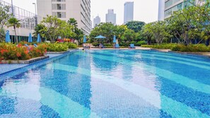 A swimming pool with clear blue water, surrounded by greenery and modern buildings. - Luxurious And Deluxe 2Br At Setiabudi Skygarden Apartment (Jakarta)