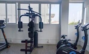 A gym with exercise equipment including a multi-functional machine and two stationary bikes. - Warm Studio Room With City View At Apartment De Prima (Medan)