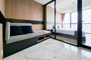 A modern hotel room with a large bed, a sofa with storage, a glass partition, and a view of the city. - Well Designed 1Br At Apartment The Smith Alam Sutera (Tangerang)