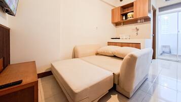 Una habitación compacta con cama, una mesita, kitchenette y baño.