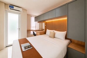 Una habitació d'hotel moderna amb un llit, una taula de treball i un armari encastrat.