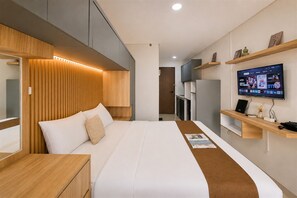 A modern hotel room with a large bed, a TV mounted on the wall, and built-in wooden cabinets. - Good And Practical Studio Room At Apartment Sudimara Forestwalk (Tangerang)