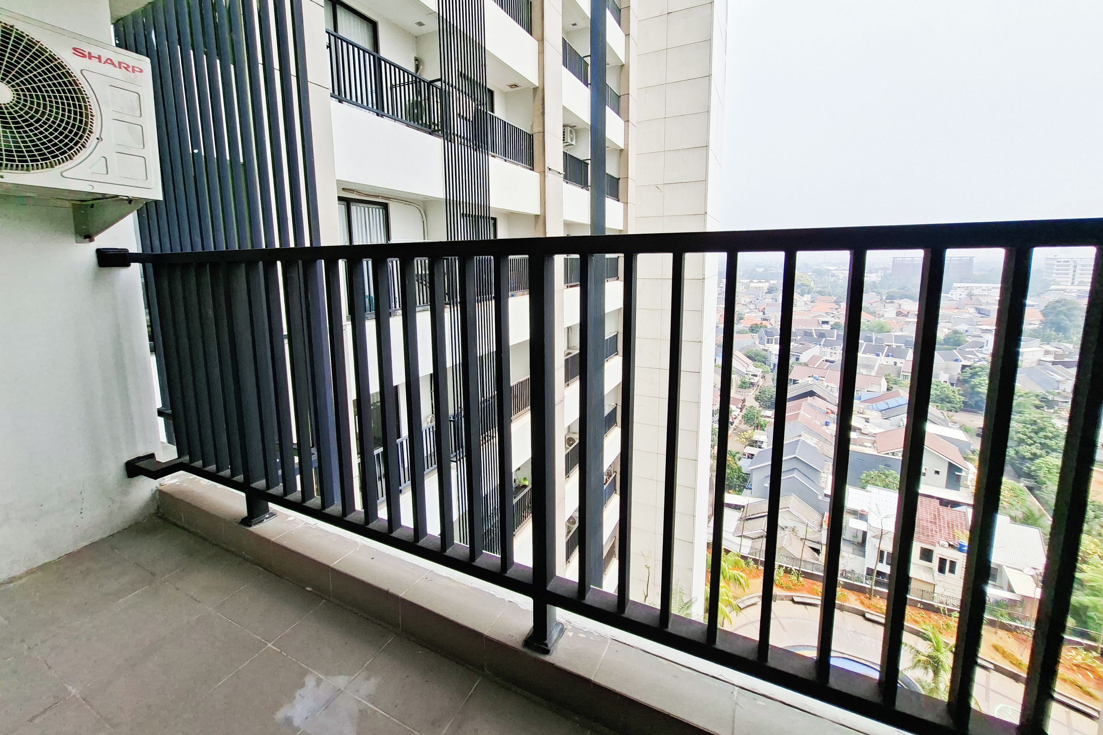 A balcony with a black metal railing, a white wall, and a view of a residential area.