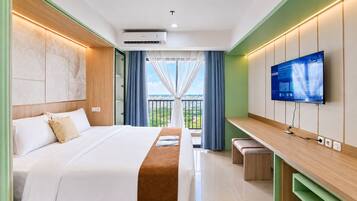 Habitación de hotel con cama, televisor montado en la pared, balcón con cortinas y vista a la ciudad.