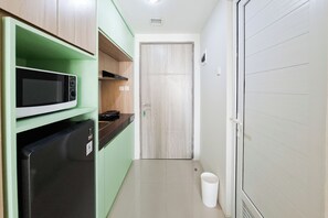 Eine schmale Küche mit einer Mikrowelle, einem Kühlschrank und einer Holztür.