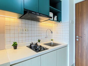 Eine Küche mit türkis-farbenen Schränken, einer Edelstahl-Spüle, einem Gasherd und einer unter der Decke angebrachten Dunstabzugshaube.
