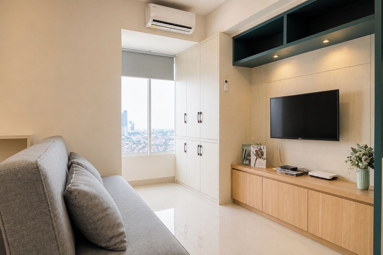 Un soggiorno moderno con un divano grigio, una TV a schermo piatto fissata al muro e vista sulla città attraverso ampie finestre.
