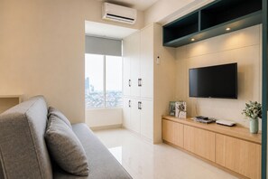 Ein modernes Wohnzimmer mit einem grauen Sofa, einem flachbildfernseher an der Wand und Blick auf die Stadt durch große Fenster.