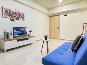 Un salon avec un canapé bleu, un téléviseur, un meuble blanc et une porte en bois.