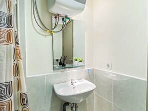 Ein Badezimmer mit einem weißen Waschbecken, einem Spiegel und einer Duschkabine mit geometrischem Muster.