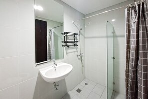 A bathroom with a white sink, a glass shower enclosure, and a mirror. - Bright And Cozy Studio At Apartment Casa De Parco (Pagedangan)