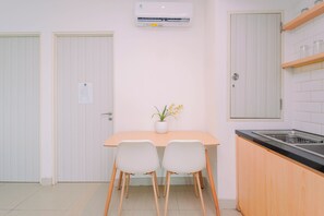 A compact kitchen with a dining table, two chairs, a potted plant, and a built-in stove. - Fresh Breezy 2Br At Apartment Grand Kamala Lagoon (Bekasi)