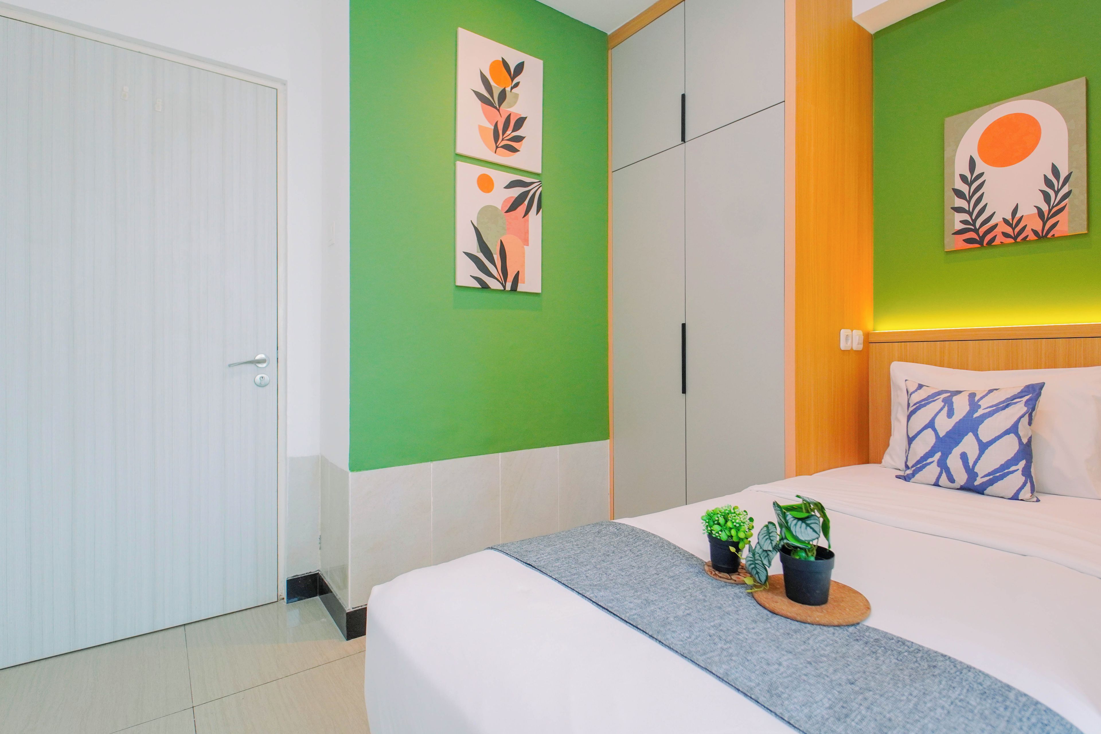 Ein Schlafzimmer mit einem Bett, zwei Zimmerpflanzen, einer Wand mit Kunstwerken und einem Kleiderschrank.