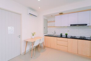 A compact kitchen with white cabinets, a black countertop, and a small dining area with two chairs. - Fresh Breezy 2Br At Apartment Grand Kamala Lagoon (Bekasi)